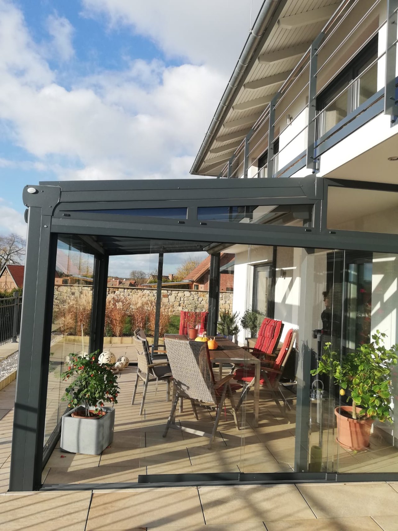Moderne Terrassenüberdachung aus Glas und Metall mit einem Esstisch und Stühlen darunter.