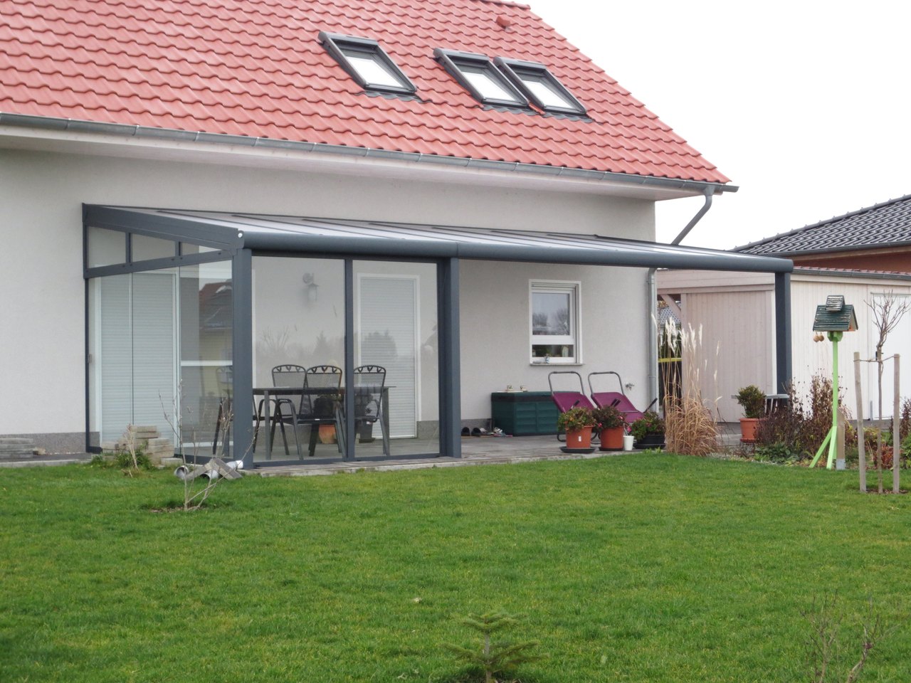 Ein modernes Wintergarten-Anbau an einem Einfamilienhaus mit rotem Dach und grünem Rasen.